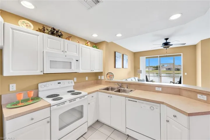 Kitchen with white appliances, a peninsula, white cabinetry, light tile patterned flooring, and light countertops