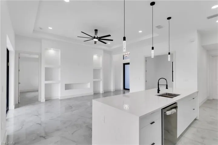 Kitchen featuring modern cabinets, light stone countertops, a raised ceiling, a kitchen island with sink, and a ceiling fan