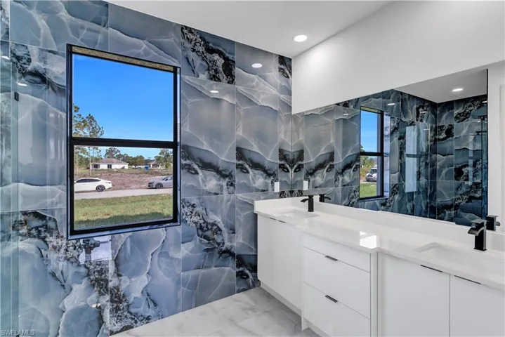 Bathroom featuring double vanity, a marble finish shower, tile walls, and light marble finish flooring