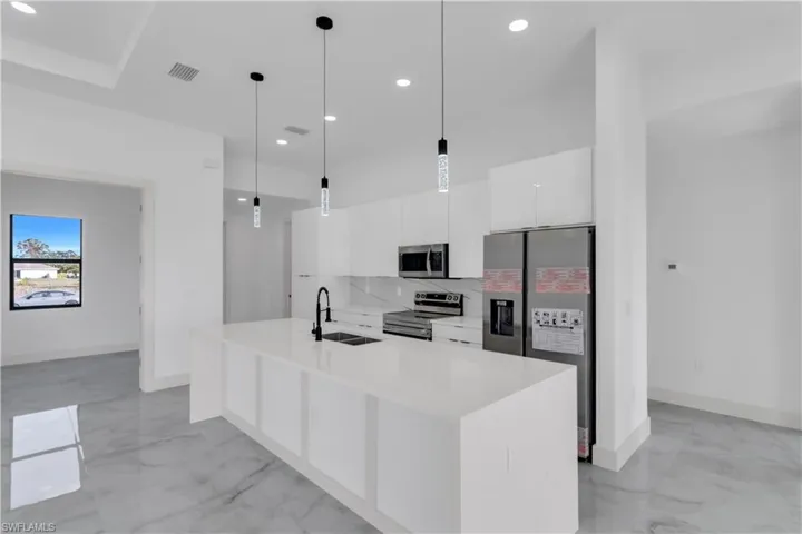 Kitchen featuring stainless steel appliances, white cabinets, a center island with sink, light stone counters, and light marble finish flooring