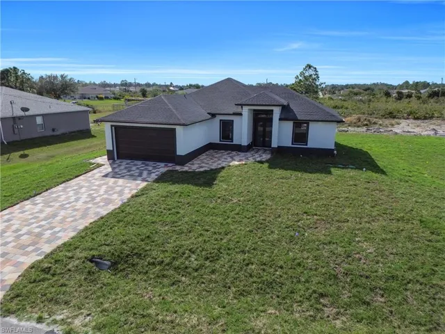 View of front of home with stucco siding, driveway, a front yard, and an attached garage