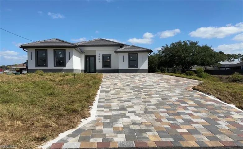 Prairie-style home with stucco siding, decorative driveway, and a tile roof