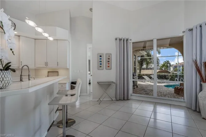 Kitchen with sink, light tile patterned floors, high vaulted ceiling, a breakfast bar, and white cabinets