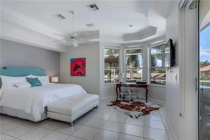 Bedroom featuring light tile patterned flooring, a raised ceiling, multiple windows, and ceiling fan