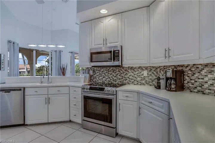 Kitchen with white cabinets, sink, light tile patterned floors, tasteful backsplash, and stainless steel appliances