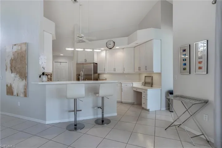 Kitchen featuring stainless steel fridge with ice dispenser, white cabinetry, a breakfast bar area, and high vaulted ceiling