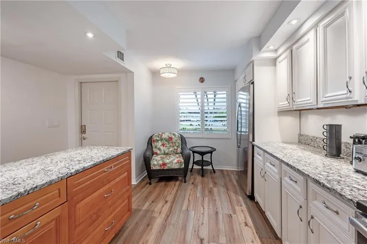Kitchen featuring light stone counters, light hardwood / wood-style floors, stainless steel fridge, and white cabinets