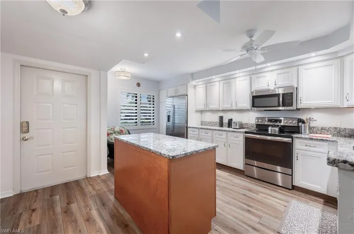 Kitchen featuring light stone counters, white cabinetry, appliances with stainless steel finishes, and light wood-type flooring