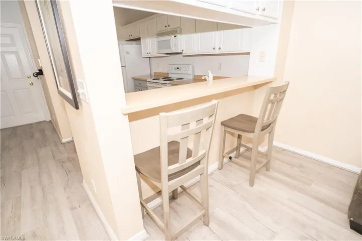 Kitchen with a kitchen breakfast bar, white appliances, light wood-style floors, and light countertops