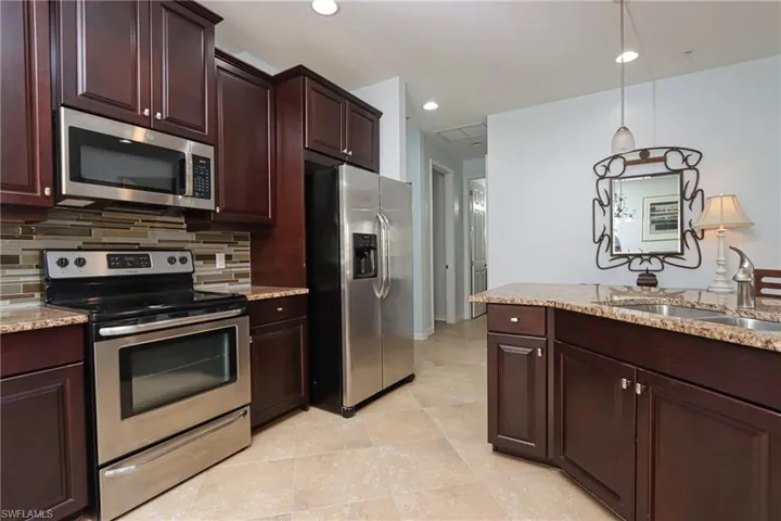 Kitchen featuring light stone countertops, pendant lighting, backsplash, stainless steel appliances, and sink