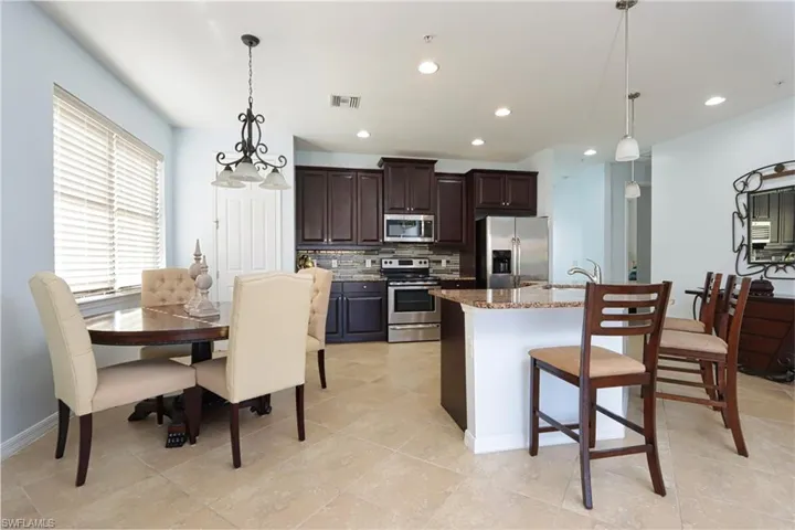 Kitchen with a center island with sink, pendant lighting, light stone countertops, and appliances with stainless steel finishes