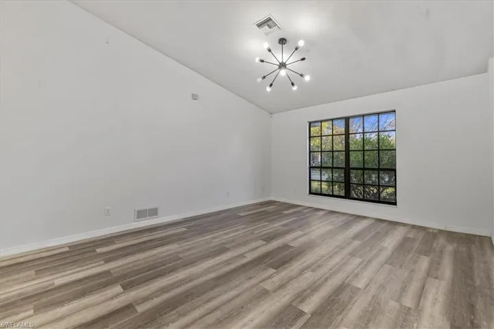 Unfurnished room with vaulted ceiling, light wood-type flooring, and a notable chandelier