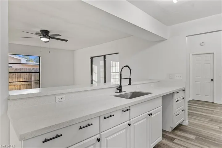 Kitchen featuring sink, white cabinetry, light stone counters, ceiling fan, and light hardwood / wood-style floors