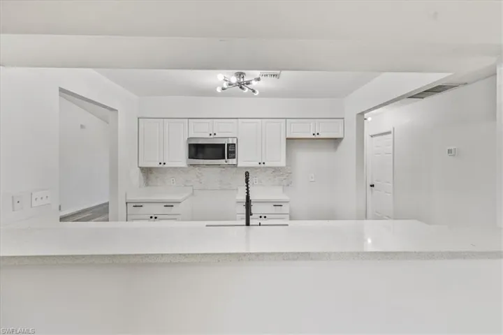 Kitchen with light stone countertops, sink, white cabinets, and backsplash