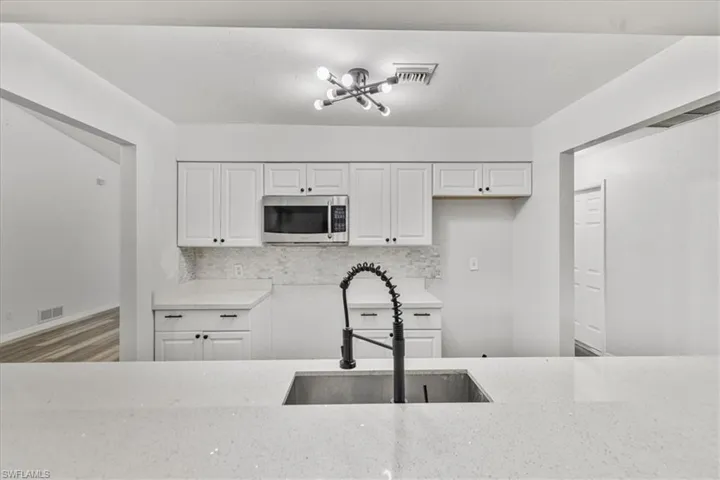 Kitchen with white cabinetry, light stone countertops, sink, and backsplash
