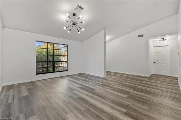 Empty room featuring hardwood / wood-style flooring, lofted ceiling, and a chandelier