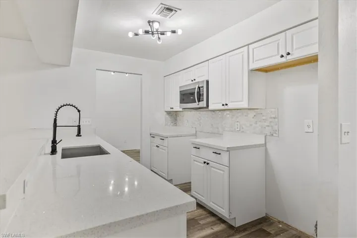 Kitchen with sink, backsplash, light stone counters, wood-type flooring, and white cabinets