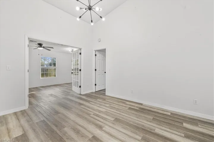 Spare room with ceiling fan with notable chandelier and light wood-type flooring
