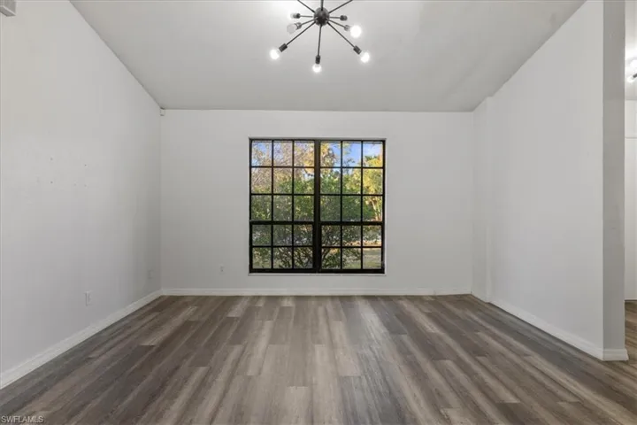 Spare room featuring lofted ceiling, dark hardwood / wood-style floors, and a notable chandelier