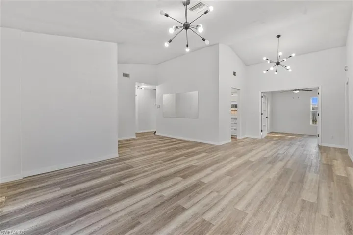 Unfurnished living room with lofted ceiling, ceiling fan with notable chandelier, and light wood-type flooring