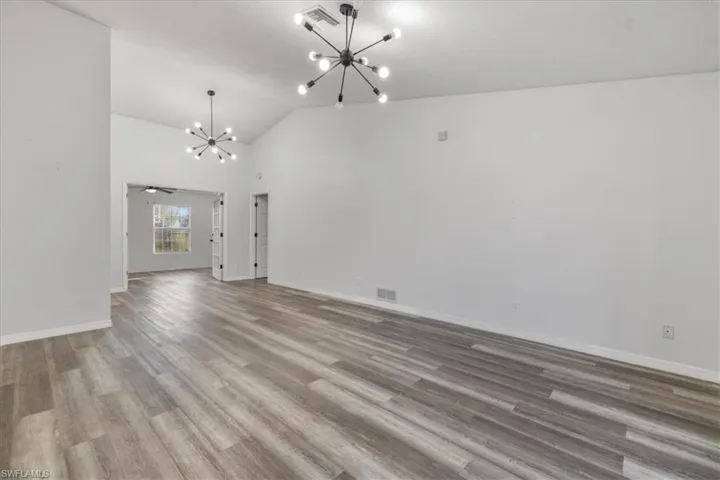 Unfurnished living room with vaulted ceiling, a chandelier, and hardwood / wood-style floors