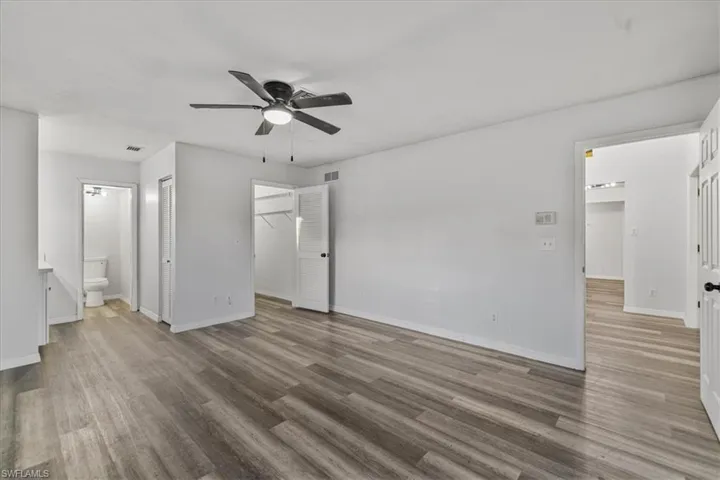 Unfurnished bedroom with ceiling fan, ensuite bathroom, hardwood / wood-style floors, and a closet