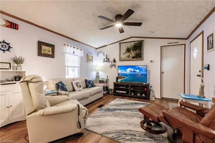 Living room featuring ceiling fan, crown molding, laminate wood-type flooring, a textured ceiling, and lofted ceiling