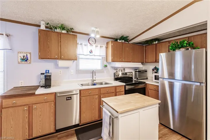 Kitchen with crown molding, newer sink/faucet, stainless steel appliances, a textured ceiling, lofted ceiling, and light wood-type laminate flooring