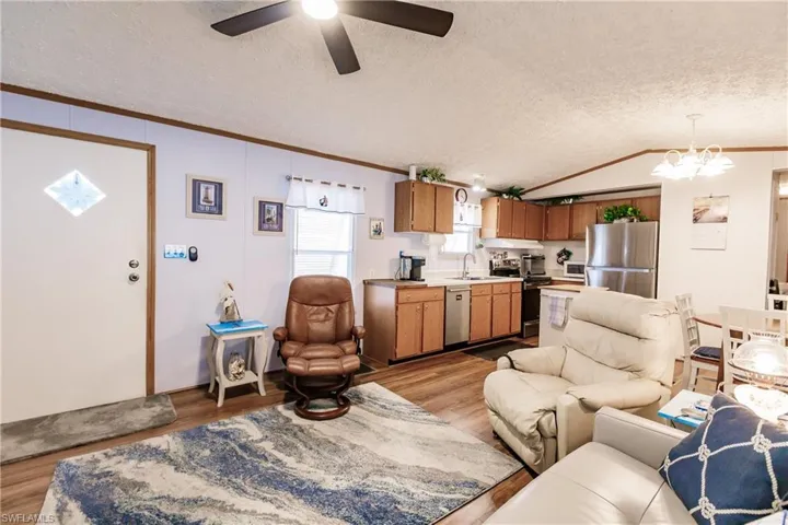 Living room with lofted ceiling, ceiling fan with light, sink, crown molding, and light laminate / wood-style flooring