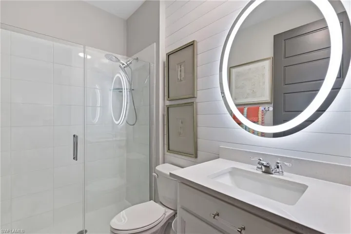 Stylish guest bath featuring a backlit mirror and glass enclosed shower