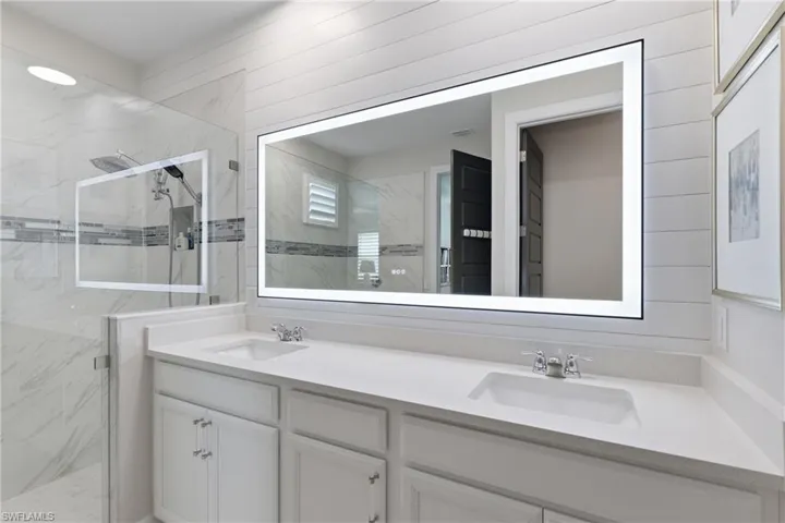 Spa-inspired owners bath with a dual vanity and frameless glass shower and elegant lighted mirror