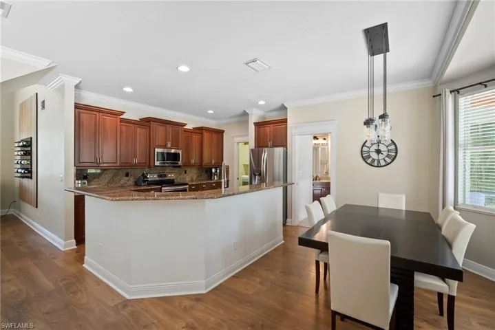Kitchen with hardwood / wood-style floors, stainless steel appliances, hanging light fixtures, crown molding, and tasteful backsplash