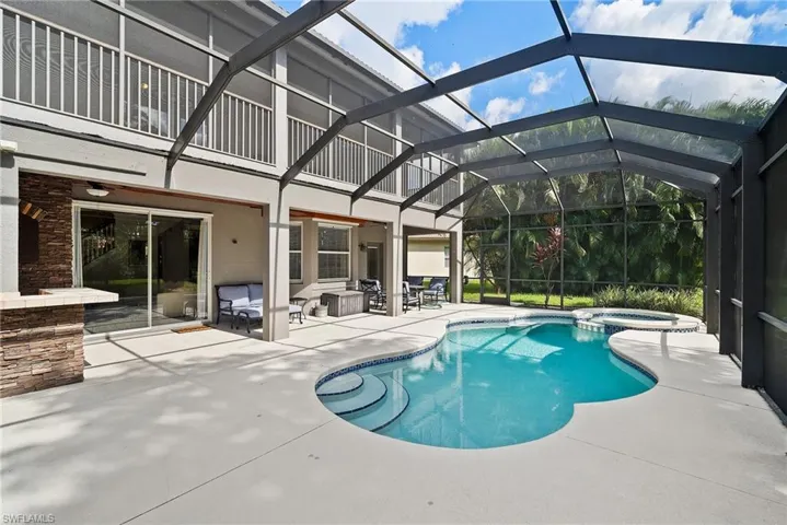 View of swimming pool with an in ground hot tub, glass enclosure, and a patio area