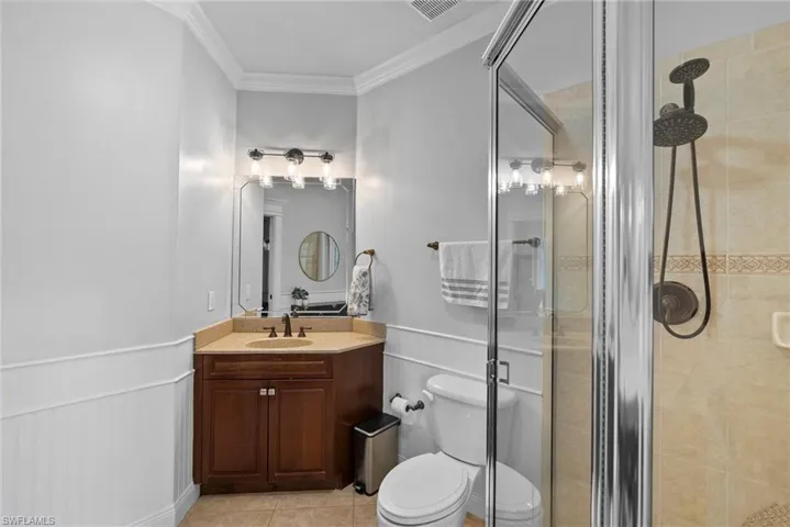 Bathroom featuring a shower with door, toilet, vanity, tile patterned flooring, and ornamental molding
