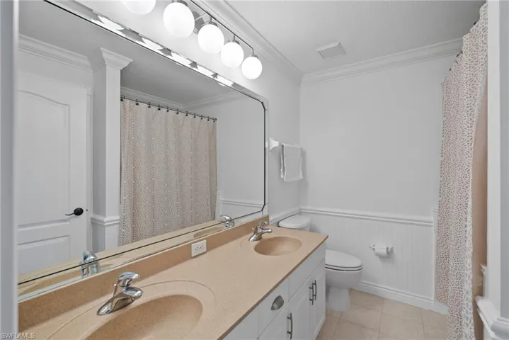 Bathroom with double sink vanity, ornamental molding, tile patterned floors, and toilet