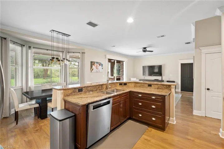 Kitchen with light hardwood / wood-style flooring, sink, stainless steel dishwasher, and decorative light fixtures