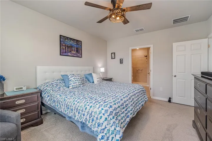 Carpeted primary bedroom featuring connected bathroom and ceiling fan light