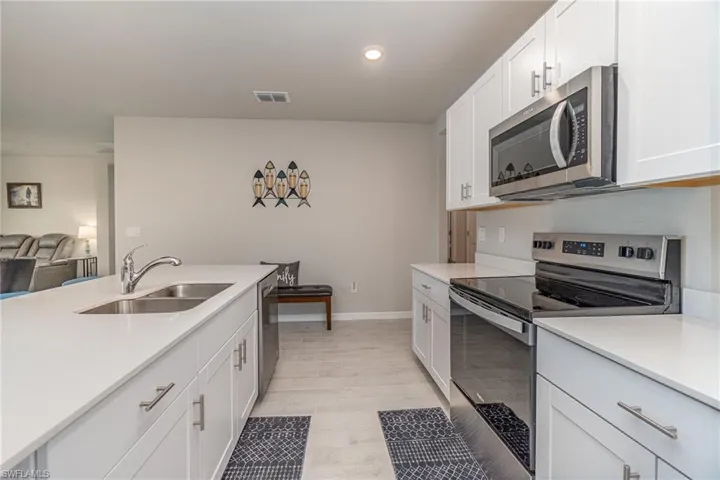 Kitchen featuring light plank tile floors, stainless steel appliances, sink, and white cabinets