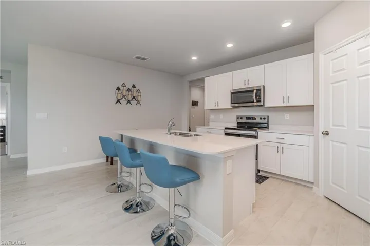 Kitchen featuring sink, an island with sink, stainless steel appliances, and white cabinetry
