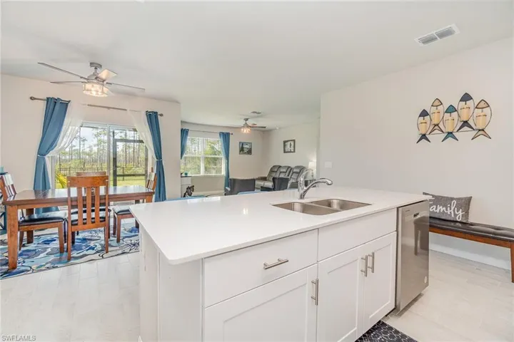 Kitchen with sink, dishwasher, ceiling fan, white cabinets, and a kitchen island with sink