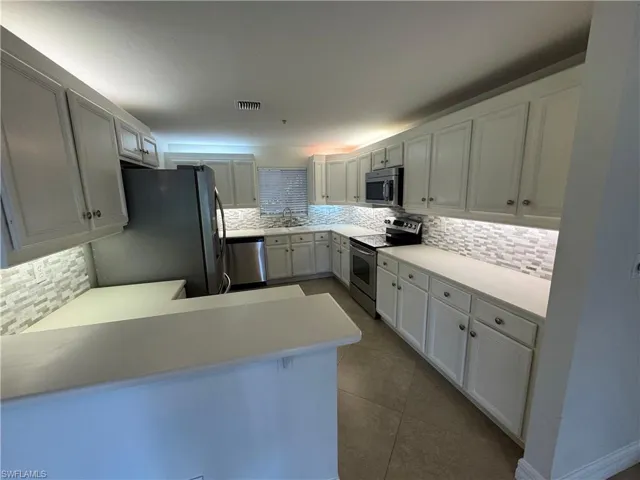 Kitchen featuring backsplash, stainless steel appliances, light countertops, a peninsula, and dark tile patterned flooring