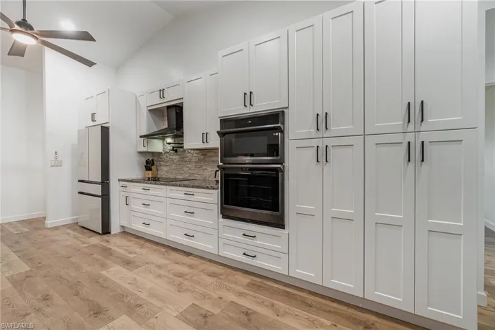 Kitchen featuring ceiling fan, white cabinets, light hardwood / wood-style flooring, wall oven, modern range hood, and black appliances