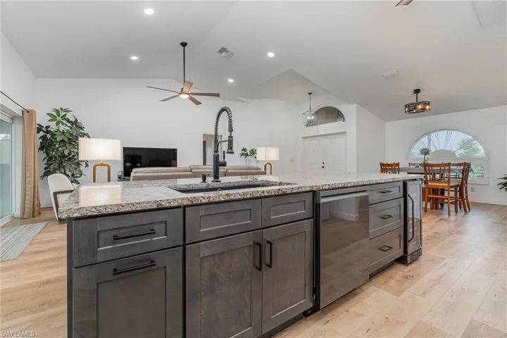 Kitchen with light hardwood / wood-style floors, a kitchen island with sink, vaulted ceiling, and ceiling fan