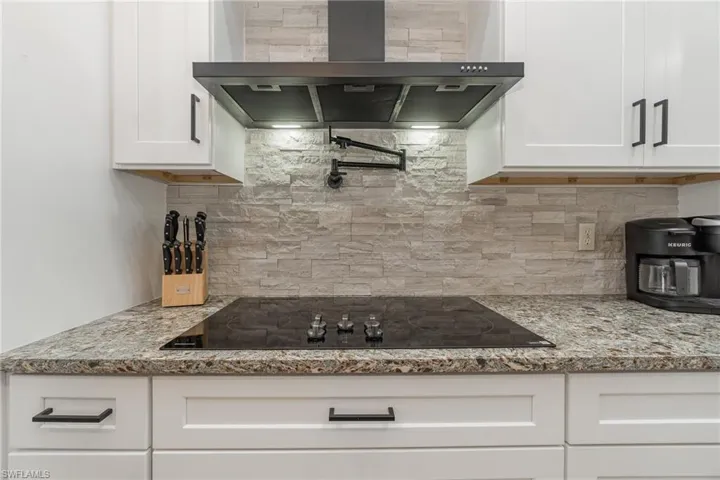 Kitchen featuring black electric cooktop, white cabinetry, backsplash, light quartz countertops, and modern range hood