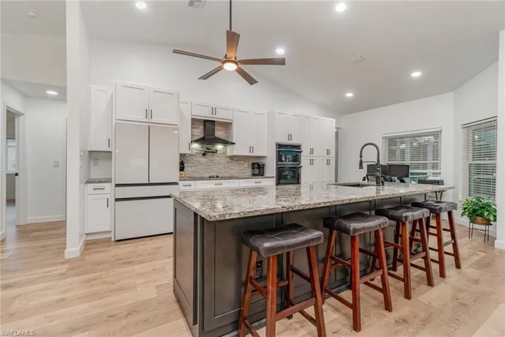 Kitchen featuring vaulted ceiling, sink, a kitchen island with sink, white cabinetry along wall, dark cabinetry on the island, and upgraded appliances