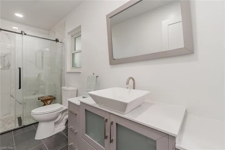 Bathroom with vanity, toilet, tile patterned floors, and a shower with galss barn door. This bath doubles as a pool bath.