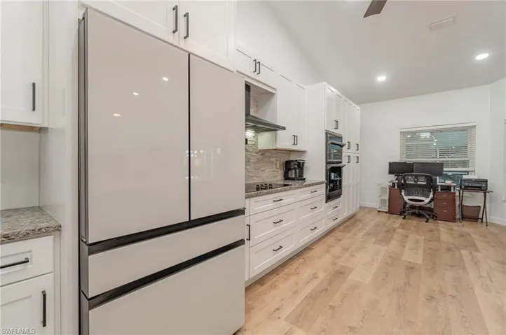 Kitchen with light hardwood / wood-style floors, white cabinets, backsplash, light stone countertops, and upgraded appliances