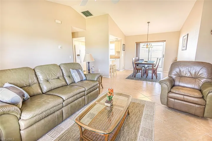 Tiled living room featuring high vaulted ceiling and ceiling fan with notable chandelier
