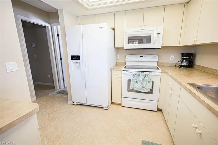 Kitchen featuring cream cabinets, light tile patterned floors, white appliances, and sink