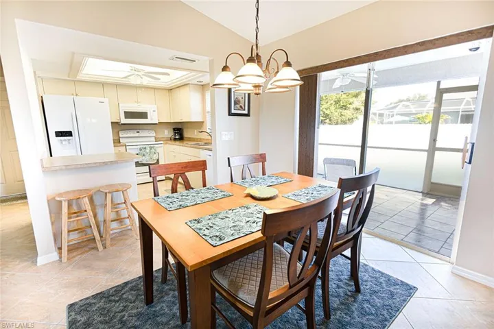 Dining area with ceiling fan with notable chandelier, light tile patterned floors, sink, and vaulted ceiling